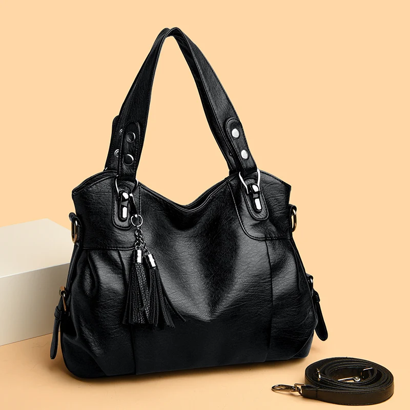 Borsa a mano in pelle nera con manici robusti, decorata con nappine e dettagli metallici, su sfondo beige. Accessorio moda elegante e versatile.