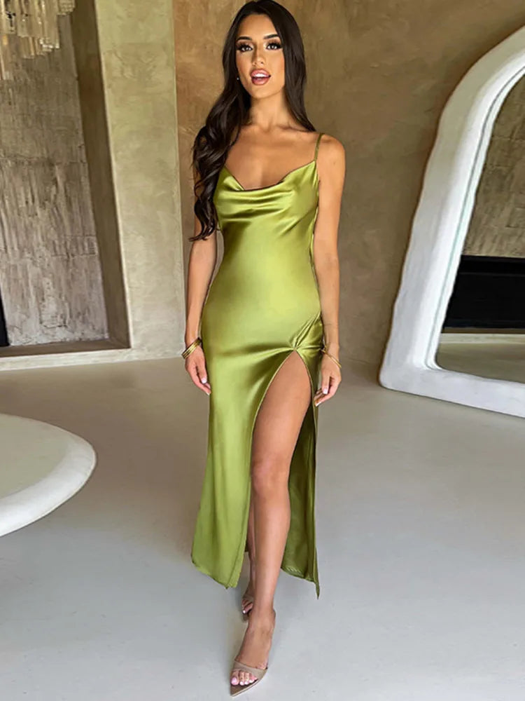 Donna in abito lungo verde satinato con spacco alto, posa in interni moderni. Moda elegante, abbigliamento da sera, tendenze 2023.