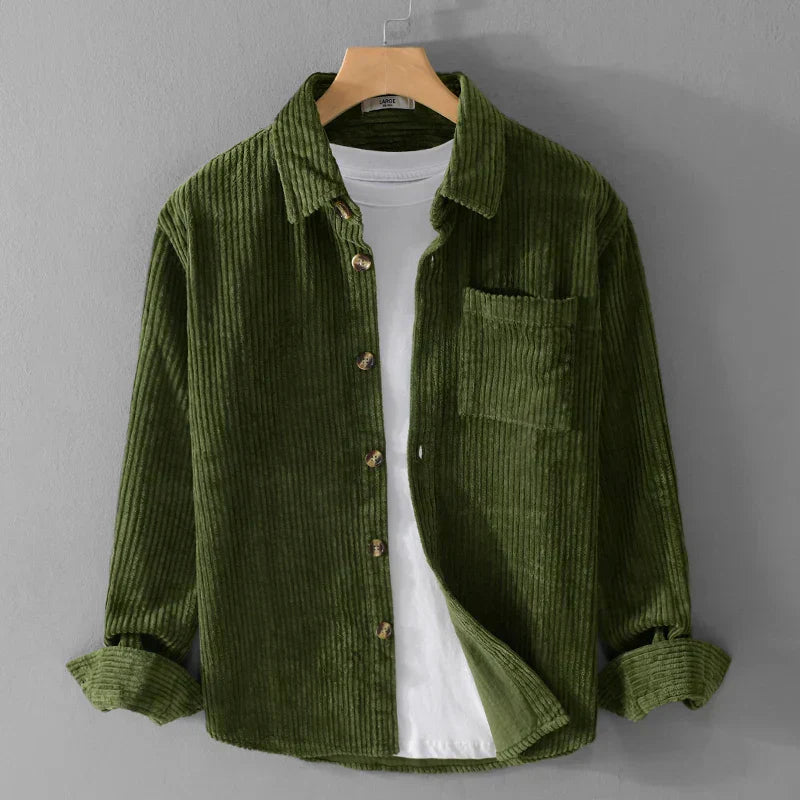 Camicia di velluto a coste verde oliva su gruccia, con tasca frontale e bottoni in legno, sopra una maglietta bianca. Moda uomo casual elegante.