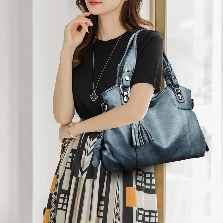 Donna con borsa a spalla in pelle blu, design elegante con frange, indossa abito nero e gonna geometrica. Accessorio moda femminile chic.