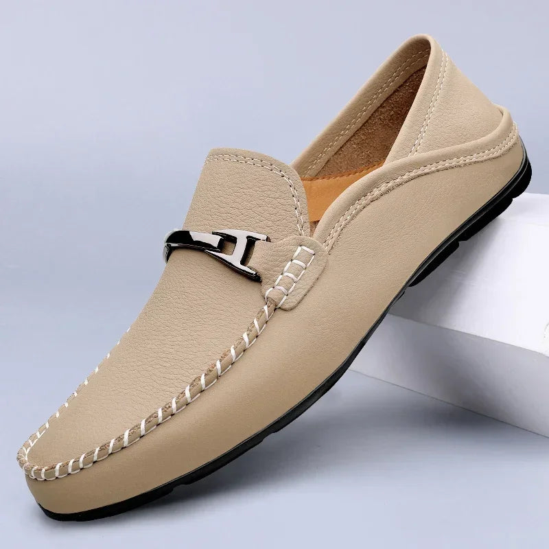 Mocassino beige da uomo in pelle, con cuciture bianche e dettaglio metallico, su sfondo grigio. Scarpe eleganti, moda maschile, calzature di lusso.