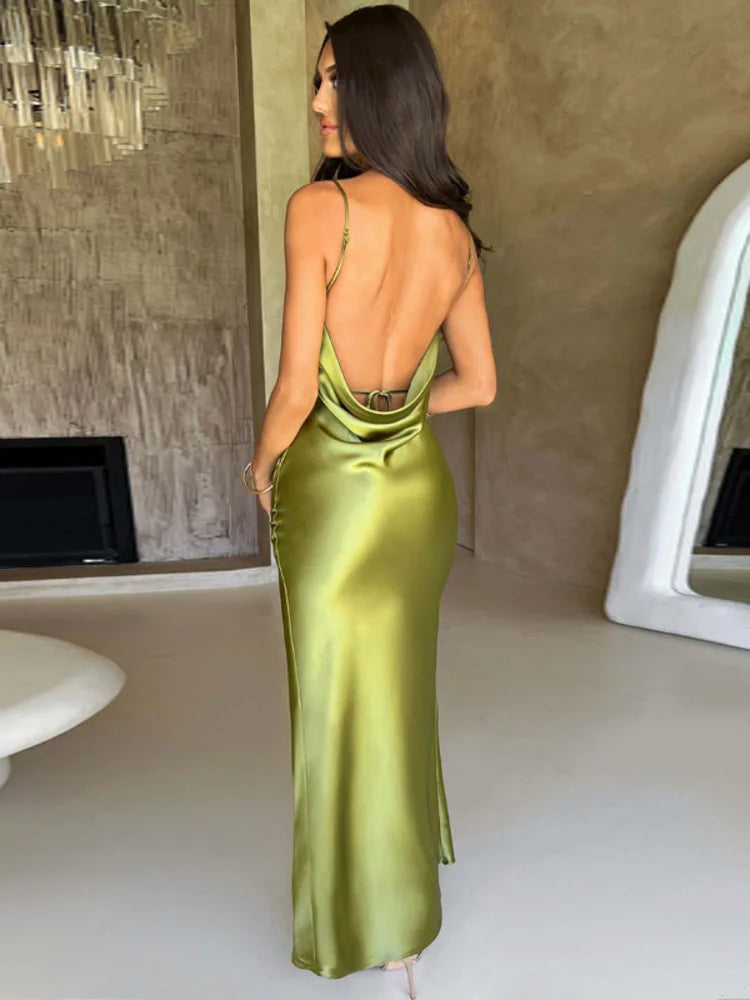 Donna in abito lungo verde satinato con schiena scoperta, in un ambiente moderno con specchio e lampadario. Eleganza, moda, abito da sera.