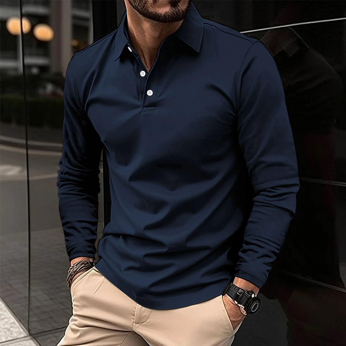 Uomo con polo blu scuro e pantaloni beige, orologio al polso, in contesto urbano moderno. Moda maschile elegante e casual.