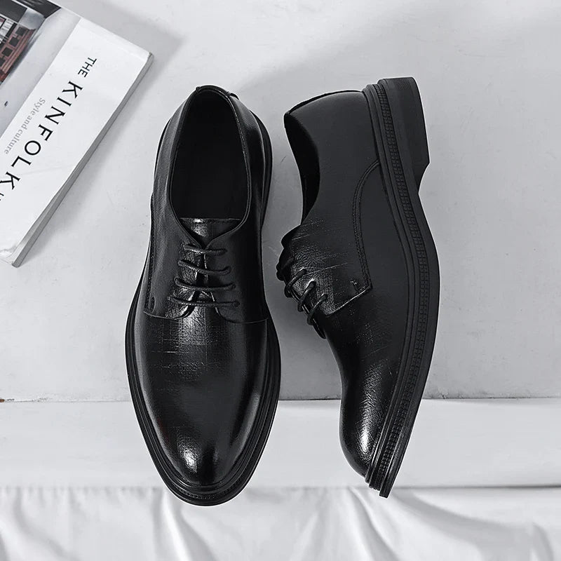 Scarpe eleganti nere in pelle lucida su sfondo bianco, con libro "The Kinfolk" accanto. Scarpe da uomo formali, moda classica, stile raffinato.
