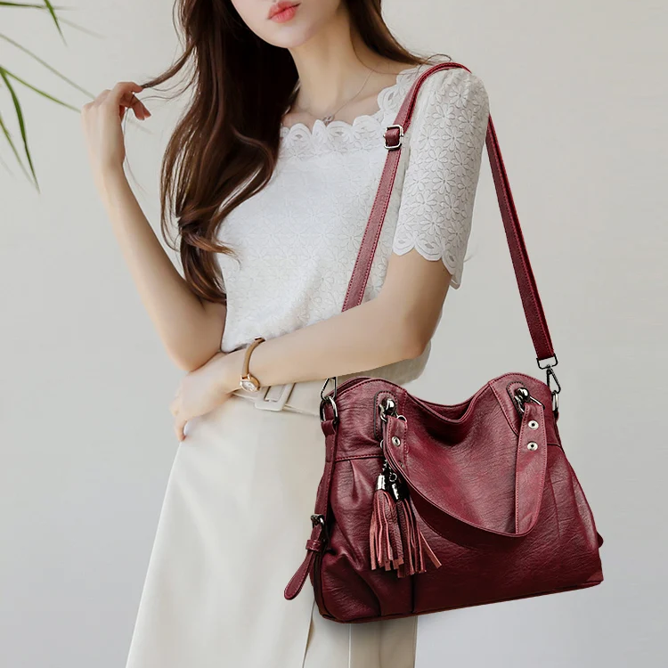 Donna con borsa a tracolla in pelle rossa, dettagli con nappe, indossa maglia bianca e gonna chiara. Accessorio moda elegante e chic.