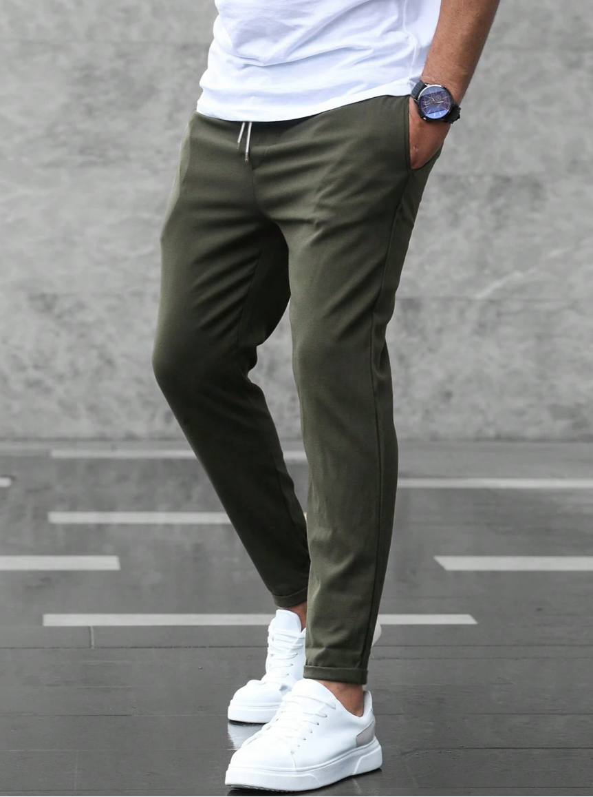 Pantaloni jogger verde oliva da uomo, abbinati a scarpe da ginnastica bianche e maglietta bianca, moda casual urbana.