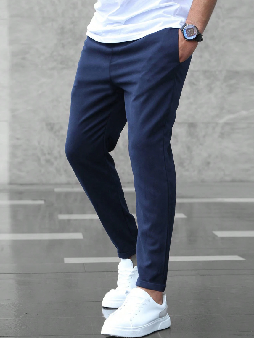 Pantaloni chino blu da uomo, abbinati a scarpe da ginnastica bianche, su sfondo grigio. Stile casual elegante, moda maschile contemporanea.