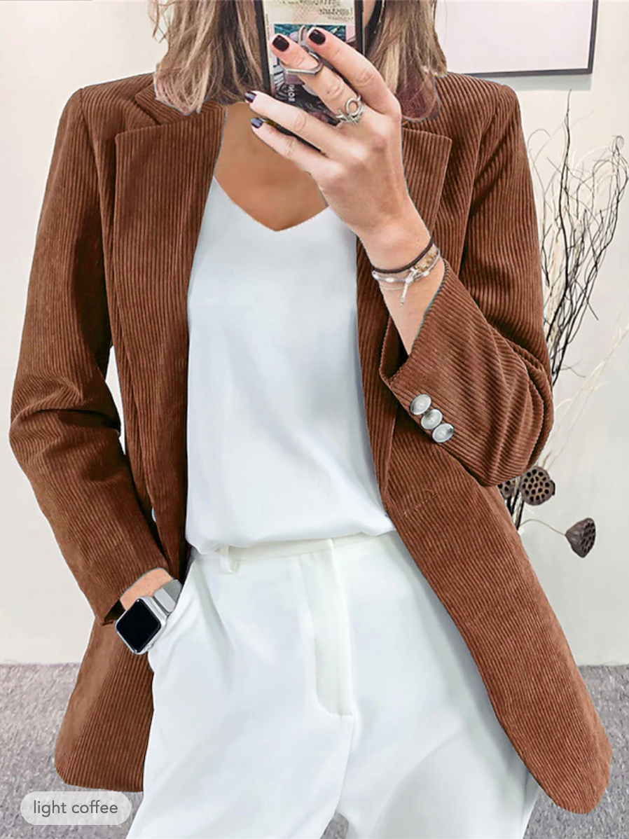 Donna con blazer marrone a coste, camicetta bianca e pantaloni coordinati. Moda elegante, abbigliamento autunnale, stile casual chic.