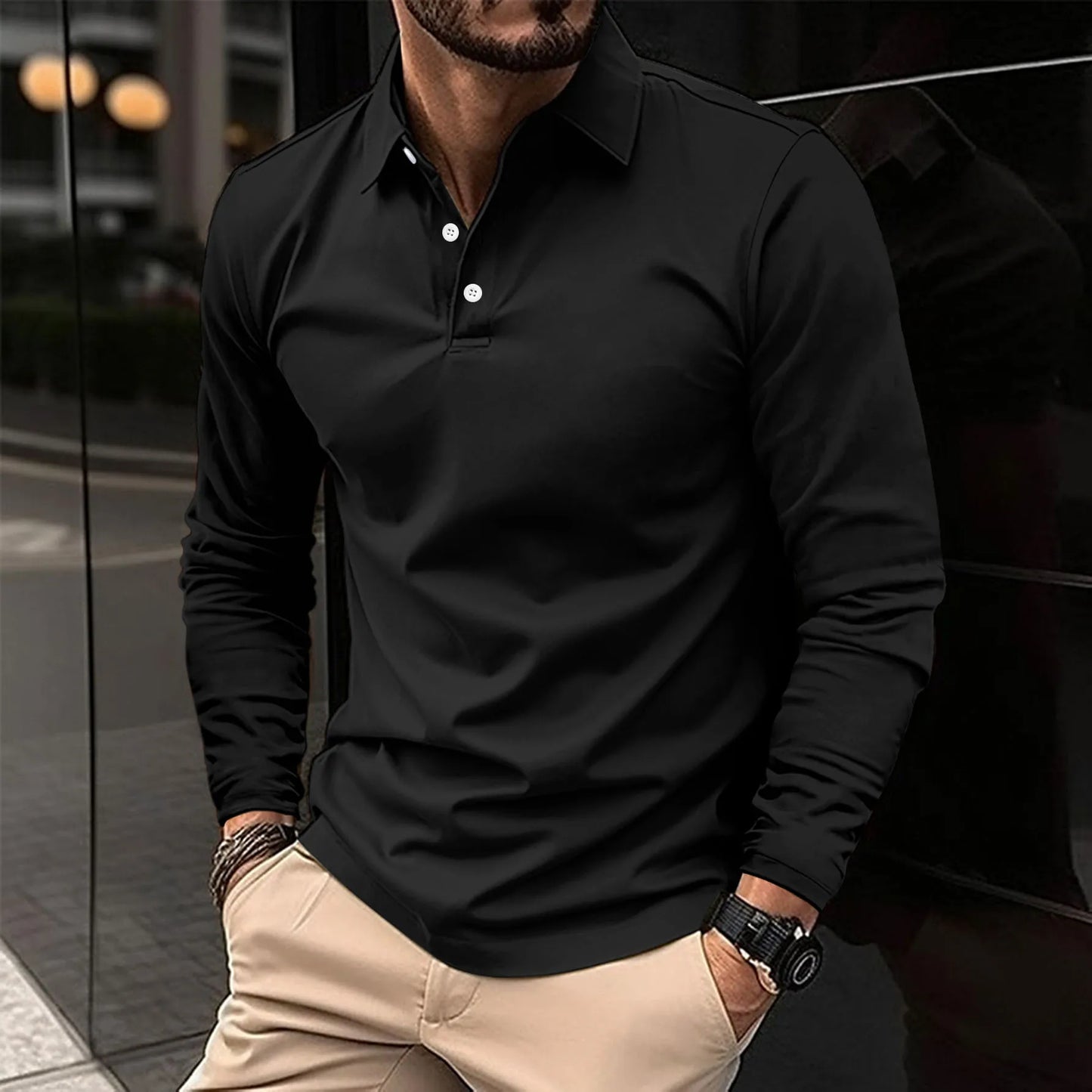 Uomo con camicia nera a maniche lunghe e pantaloni beige, orologio al polso, in piedi davanti a un edificio moderno. Moda maschile elegante.