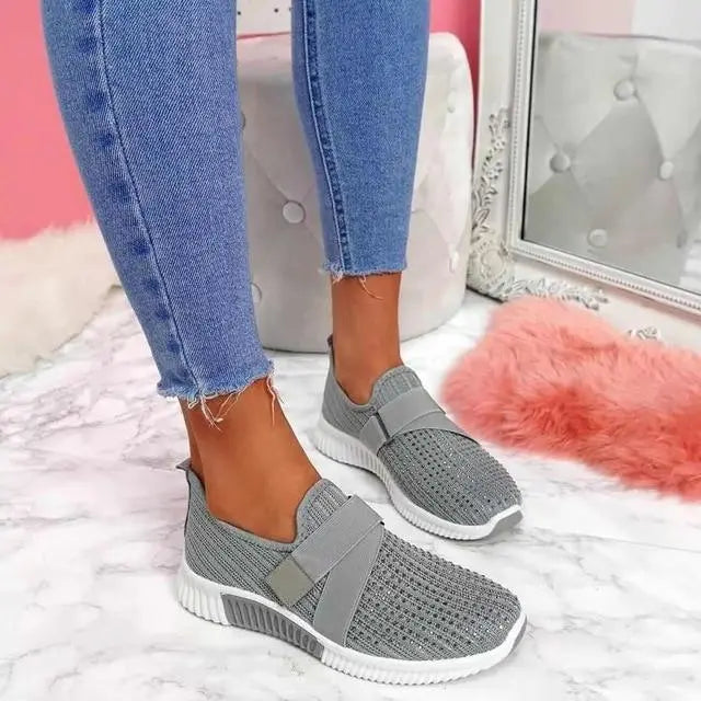 Scarpe da ginnastica grigie in maglia su pavimento in marmo, indossate con jeans aderenti. Design moderno e comodo, perfetto per look casual.
