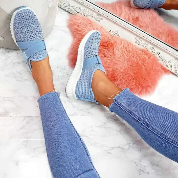Scarpe da ginnastica blu su pavimento in marmo, accanto a tappeto rosa e specchio decorativo. Moda casual, jeans strappati, stile moderno.