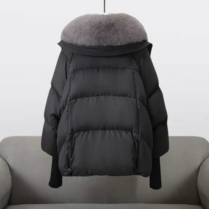 Giacca invernale nera con collo in pelliccia grigia, design imbottito, appesa su sfondo chiaro. Moda donna, abbigliamento caldo, stile elegante.