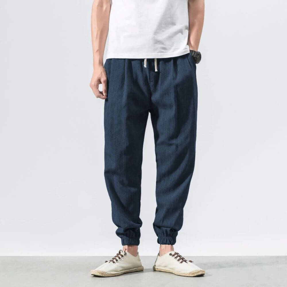 Pantaloni jogger uomo in denim blu, stile casual, con elastico alla caviglia. Indossati con scarpe bianche e maglietta bianca.