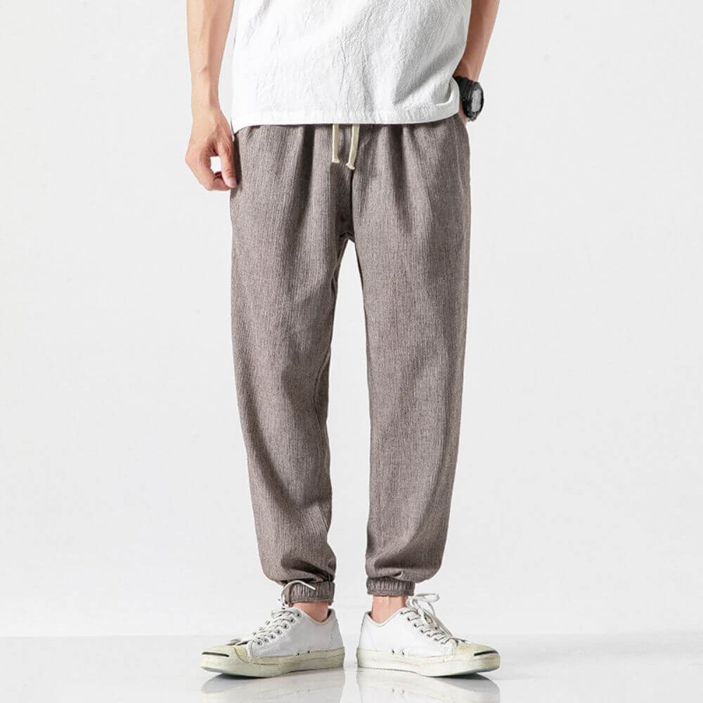 Pantaloni jogger uomo in lino grigio, stile casual, abbinati a scarpe da ginnastica bianche e maglietta bianca. Outfit moda maschile.