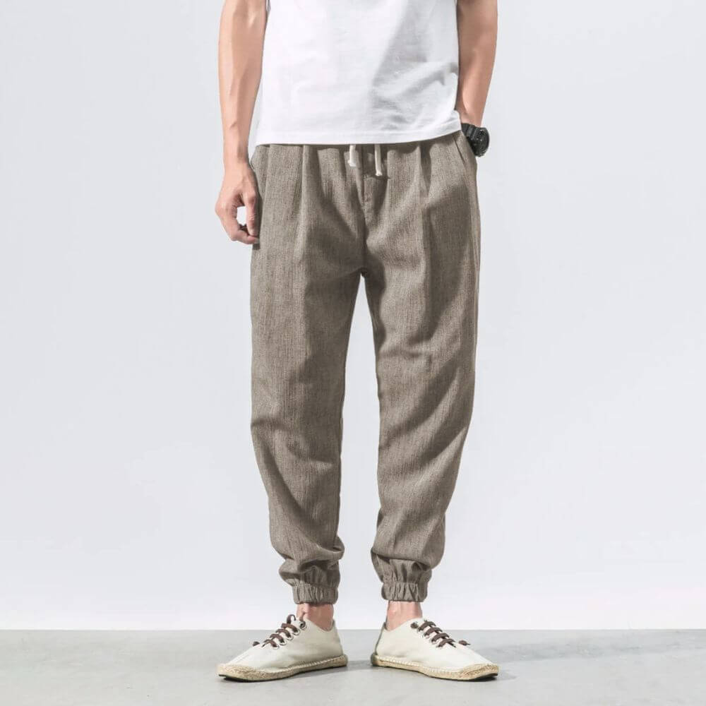 Pantaloni jogger uomo in lino beige, stile casual, con elastico alla caviglia. Indossati con t-shirt bianca e scarpe sportive bianche.
