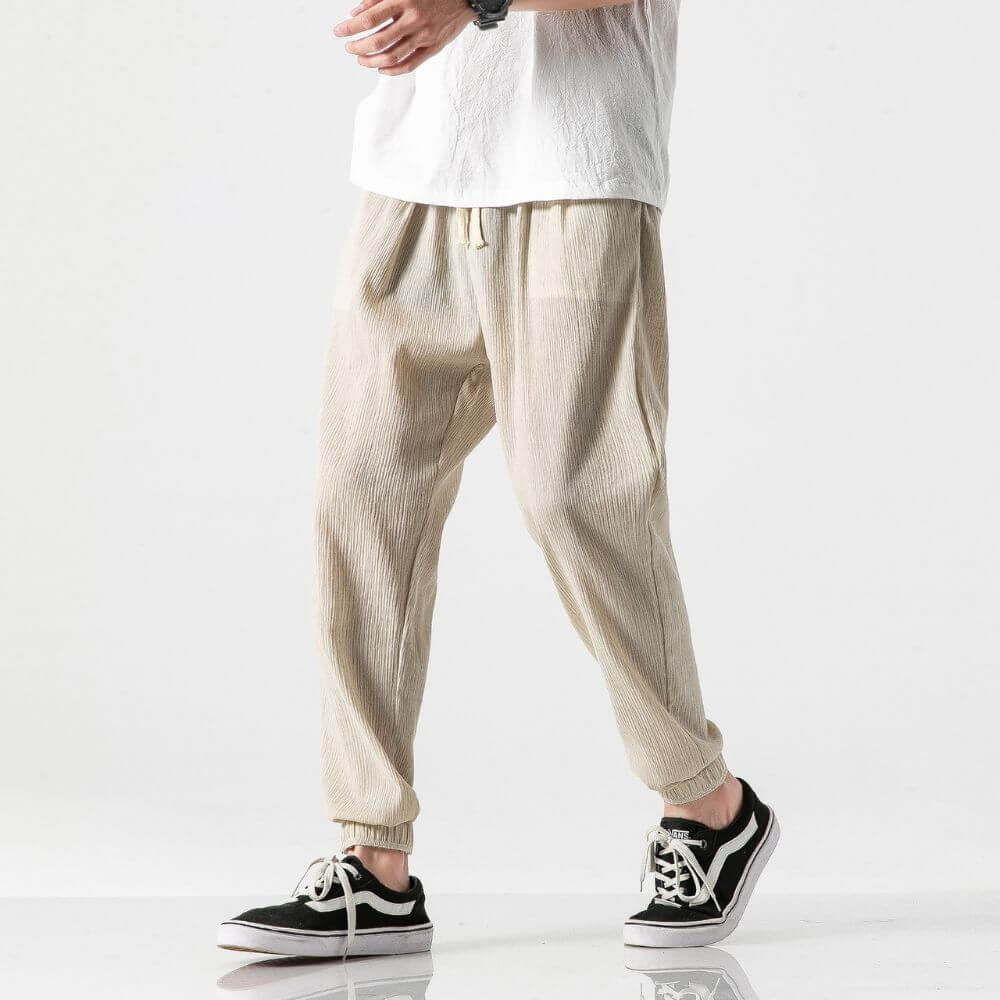 Pantaloni beige in lino, stile casual, indossati con scarpe da ginnastica nere e bianche, su sfondo bianco. Moda uomo, abbigliamento estivo.