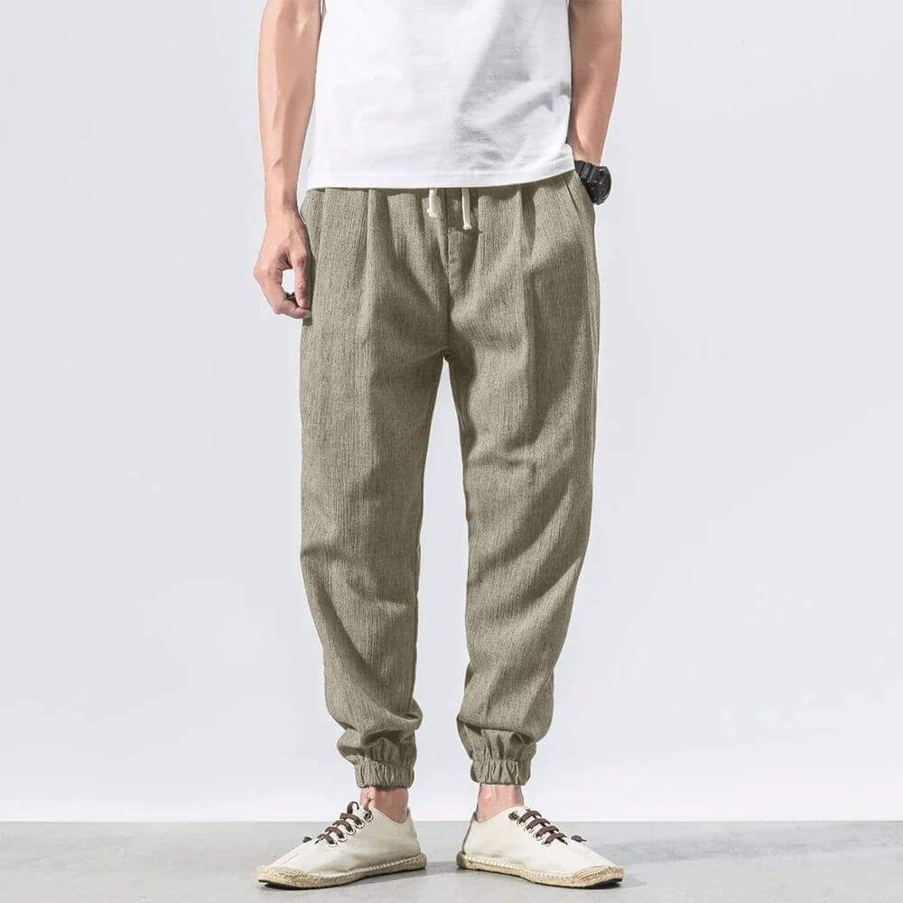 Pantaloni jogger uomo in lino beige, stile casual, con elastico alla caviglia. Indossati con t-shirt bianca e scarpe casual.