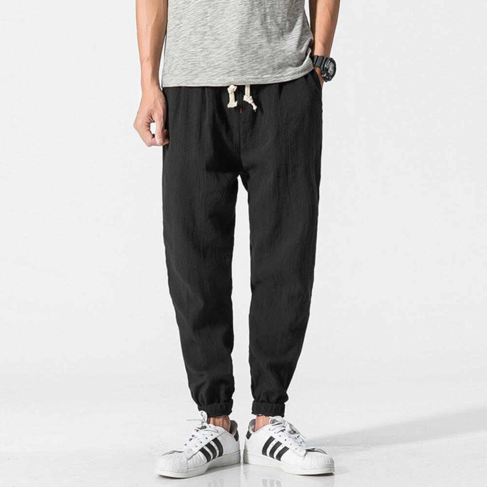 Pantaloni jogger neri da uomo, tessuto leggero, abbinati a scarpe da ginnastica bianche e maglietta grigia. Stile casual e moderno.