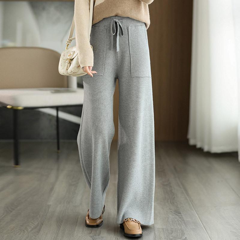 Pantaloni grigi larghi in maglia, indossati con maglione beige e borsa a tracolla, su pavimento in legno chiaro. Moda casual autunnale.