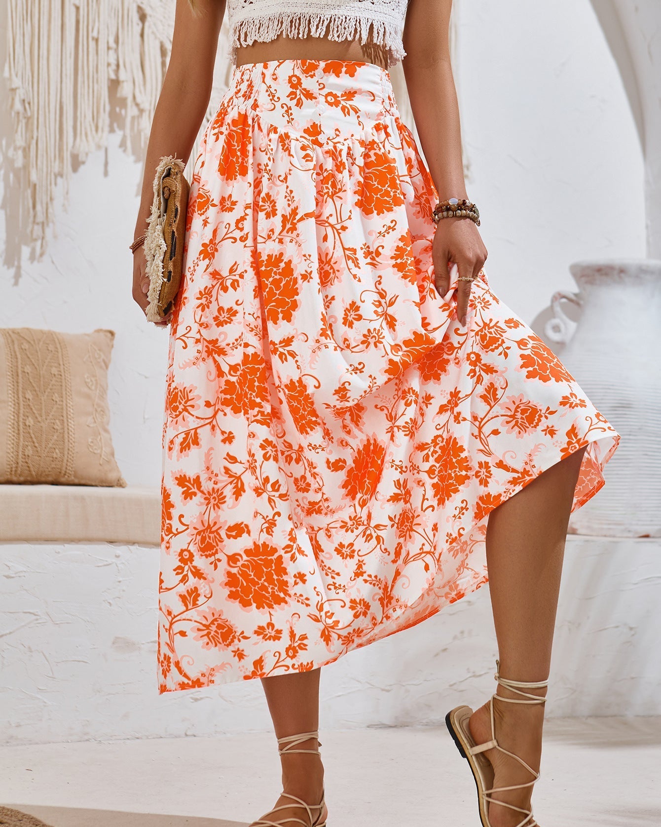 Gonna lunga estiva a fiori arancioni, indossata con sandali e top bianco, stile boho chic. Accessori: borsa intrecciata, bracciali.