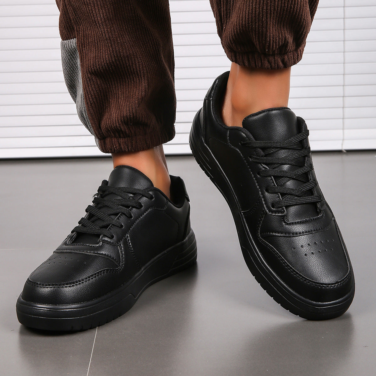 Scarpe da ginnastica nere in pelle, design moderno, suola robusta, indossate con pantaloni marroni. Scarpe sportive eleganti per uomo.