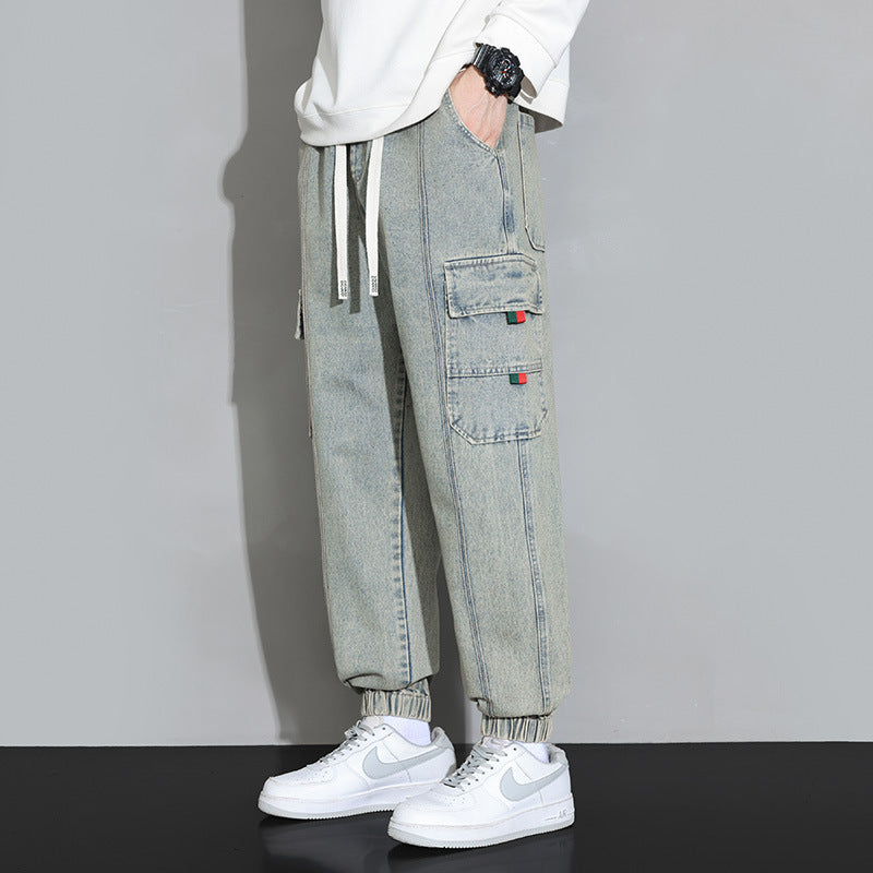 Pantaloni cargo uomo in denim chiaro, tasche laterali, abbinati a sneakers bianche Nike. Stile casual, moda streetwear, abbigliamento trendy.