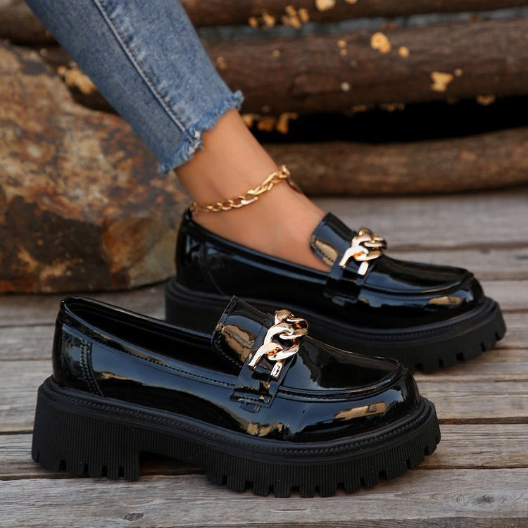 Scarpe mocassini neri lucidi con catena dorata, suola spessa e jeans strappati. Moda autunnale, calzature eleganti, stile casual chic.