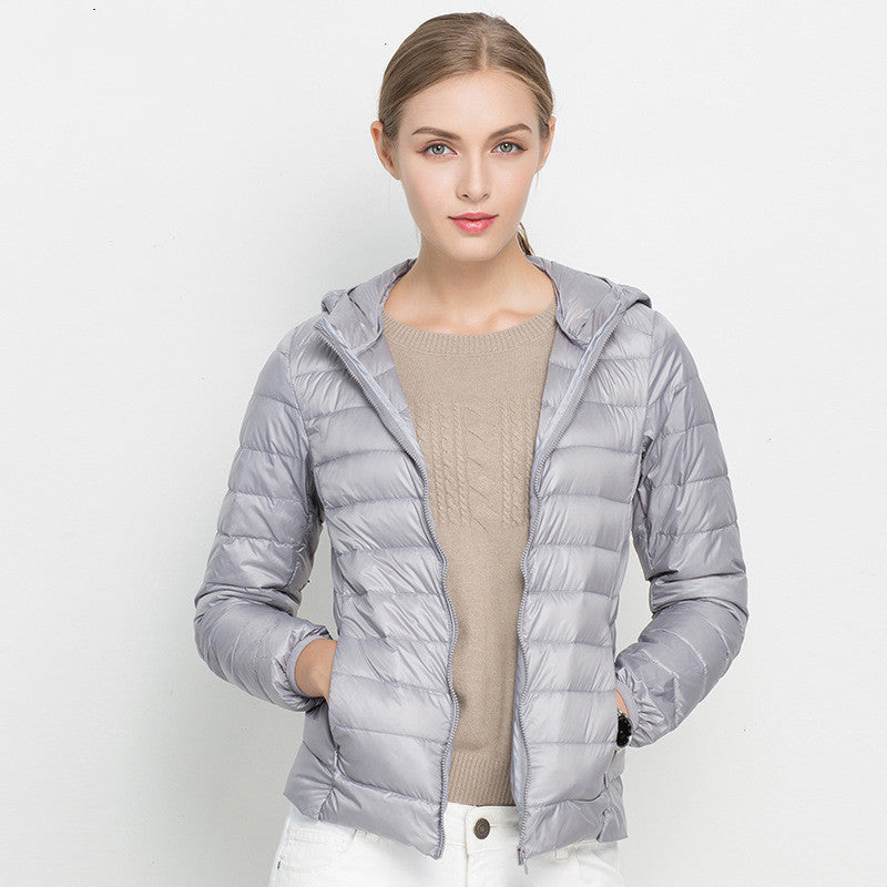 Giacca piumino donna grigia con cappuccio, indossata su maglione beige. Moda invernale, abbigliamento casual, stile elegante e moderno.