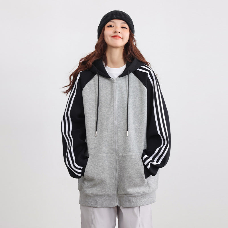 Donna sorridente con felpa grigia e nera con cappuccio, strisce bianche sulle maniche, indossa berretto nero. Moda casual, abbigliamento sportivo.
