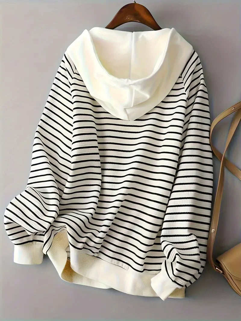Felpa a righe bianche e nere con cappuccio, appesa su gruccia. Moda casual, abbigliamento donna, stile autunnale.