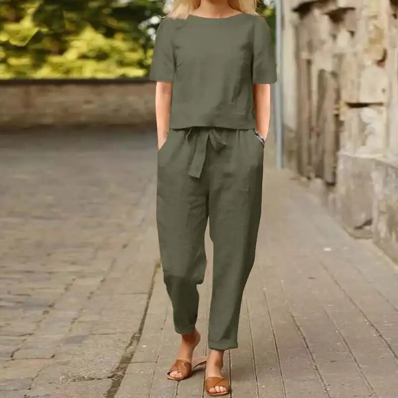 Donna in tuta verde oliva, maniche corte, cammina su strada lastricata. Moda casual estiva, abbigliamento comodo, sandali marroni.