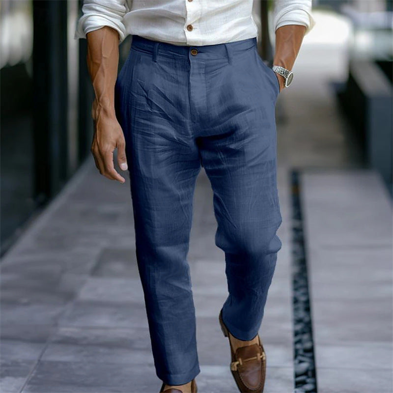 Uomo in camicia bianca e pantaloni blu eleganti, cammina su marciapiede. Indossa mocassini marroni e orologio, stile casual chic.