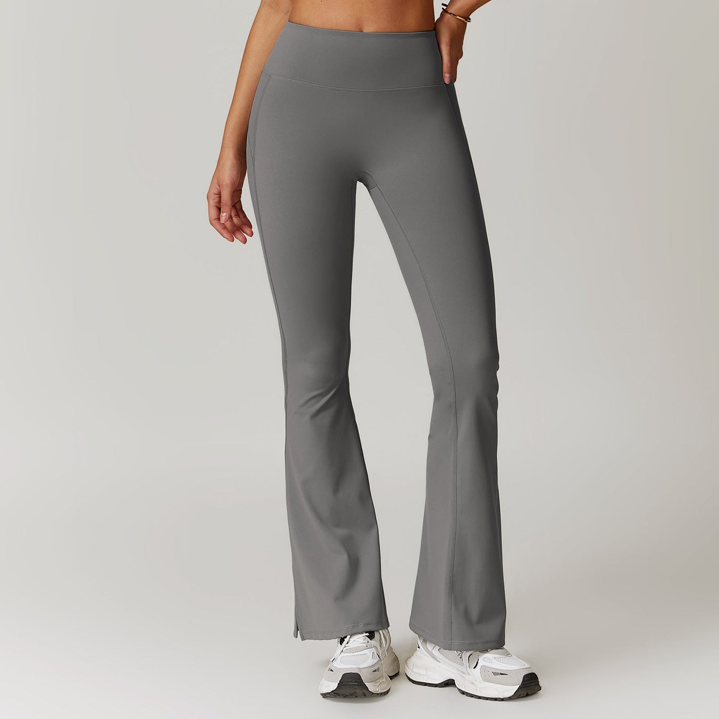 Pantaloni yoga grigi a zampa, vita alta, indossati da una donna, abbinati a scarpe da ginnastica bianche. Abbigliamento sportivo femminile elegante.