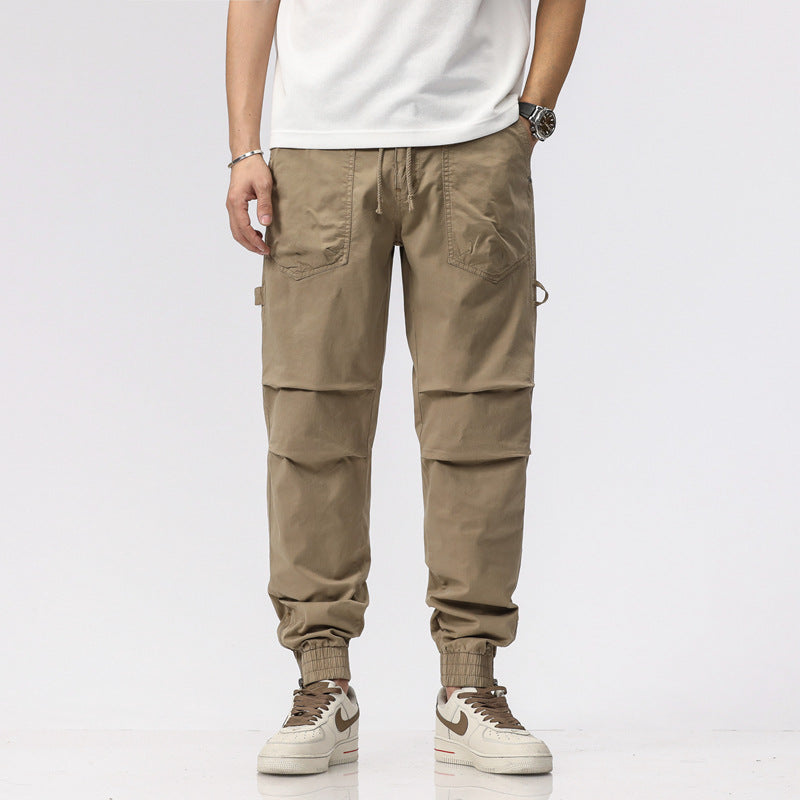Pantaloni cargo uomo beige, tasche multiple, stile casual, abbinati a scarpe sportive bianche e marroni, moda streetwear maschile.