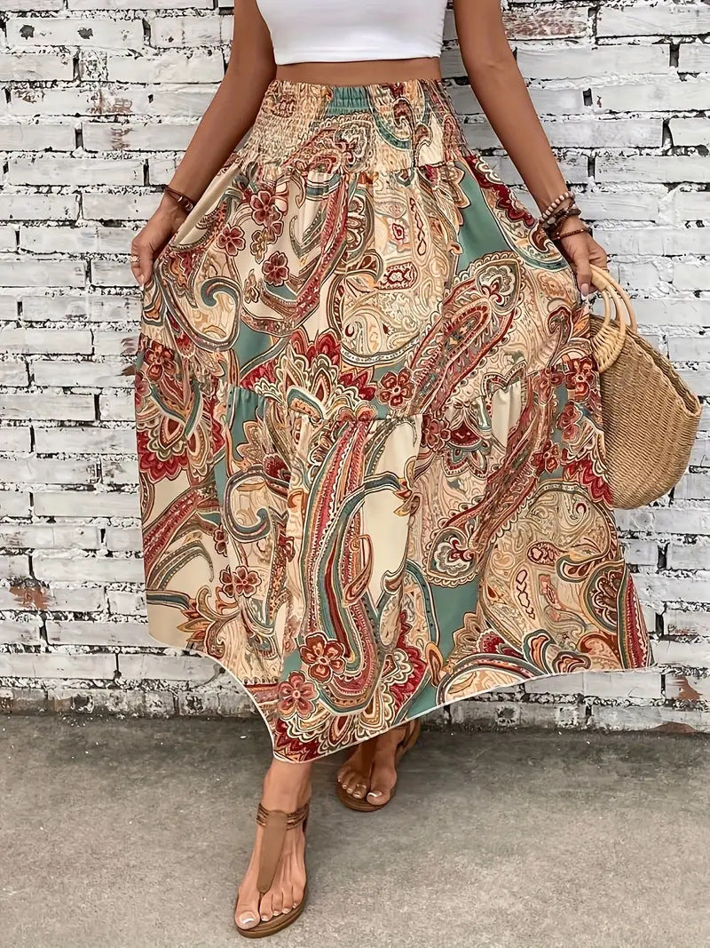 Gonna lunga boho con stampa paisley multicolore, indossata da donna con top bianco. Moda estiva casual, sandali marroni, borsa di paglia.