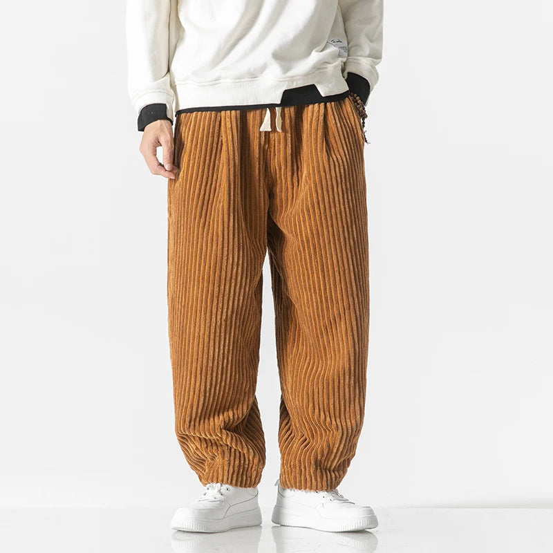 Pantaloni a coste marroni da uomo, stile casual, indossati con felpa bianca e scarpe da ginnastica bianche. Moda autunnale, abbigliamento comodo.