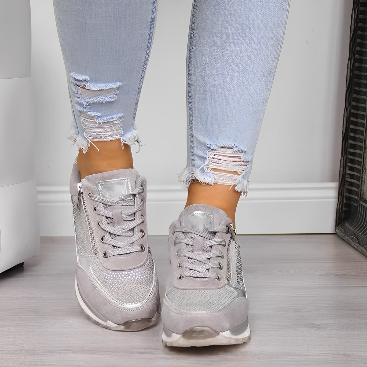 Scarpe da ginnastica grigie scintillanti su pavimento in legno, indossate con jeans strappati chiari. Moda casual, calzature trendy, stile urbano.