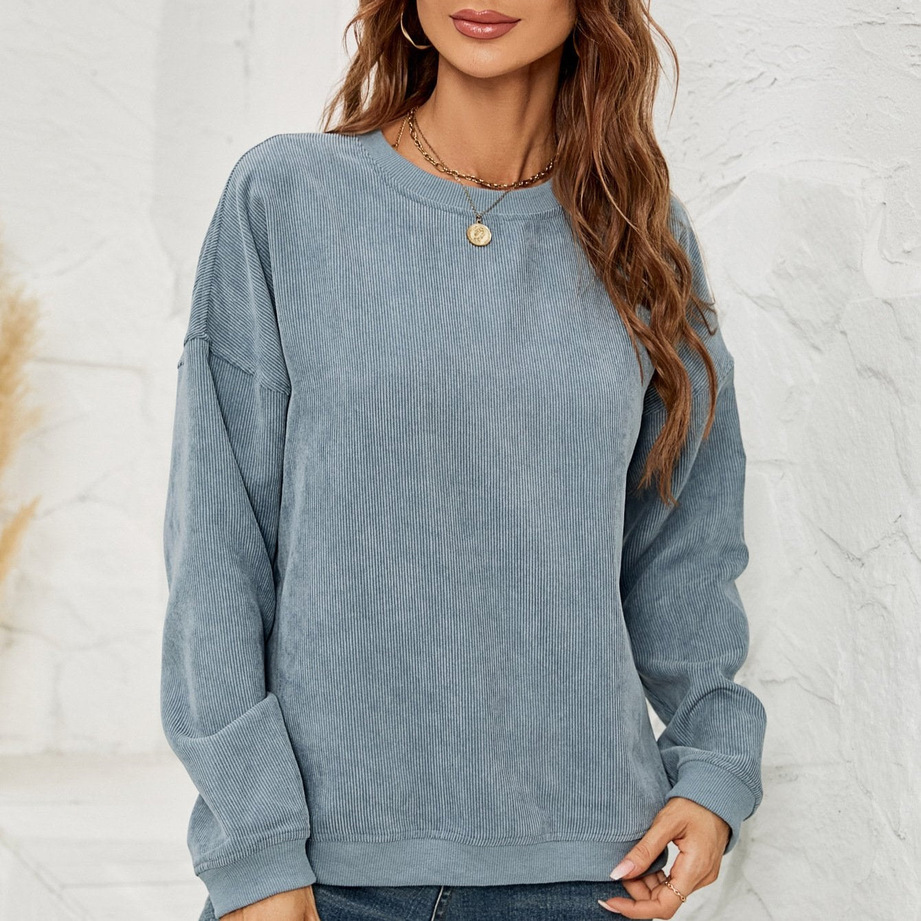 Donna con maglione blu a coste, capelli castani ondulati, collana dorata, sfondo bianco. Moda casual autunnale, abbigliamento femminile trendy.