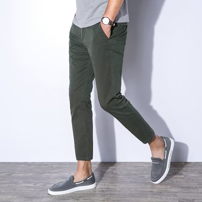 Uomo con pantaloni chino verde scuro, maglietta grigia e mocassini grigi. Moda casual maschile, stile moderno, abbigliamento quotidiano.