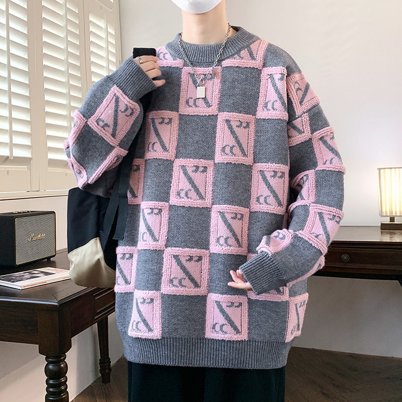 Maglione oversize grigio e rosa con motivo geometrico, indossato da una persona in una stanza moderna. Arredamento minimalista sullo sfondo.