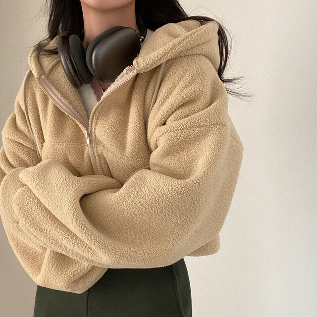 Giacca in pile beige con cappuccio, indossata da una persona con cuffie nere al collo. Moda autunnale, abbigliamento casual caldo e confortevole.