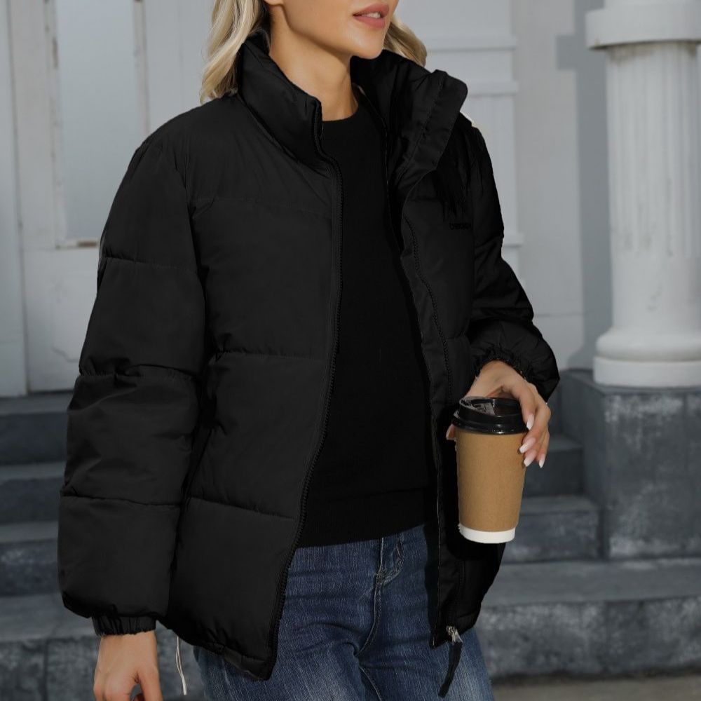 Donna con giacca nera imbottita, jeans blu, tiene caffè da asporto. Moda invernale casual, abbigliamento caldo, stile urbano.