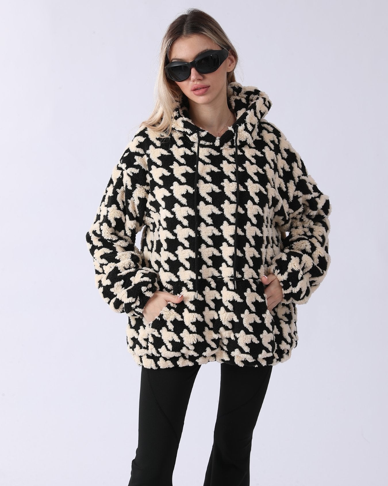 Donna con occhiali da sole indossa felpa oversize a quadri pied de poule bianco e nero, moda autunno inverno, stile casual chic.