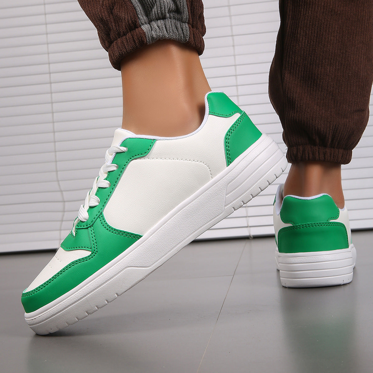 Scarpe da ginnastica bianche e verdi su pavimento grigio, indossate da una persona con pantaloni marroni. Design moderno, moda casual.