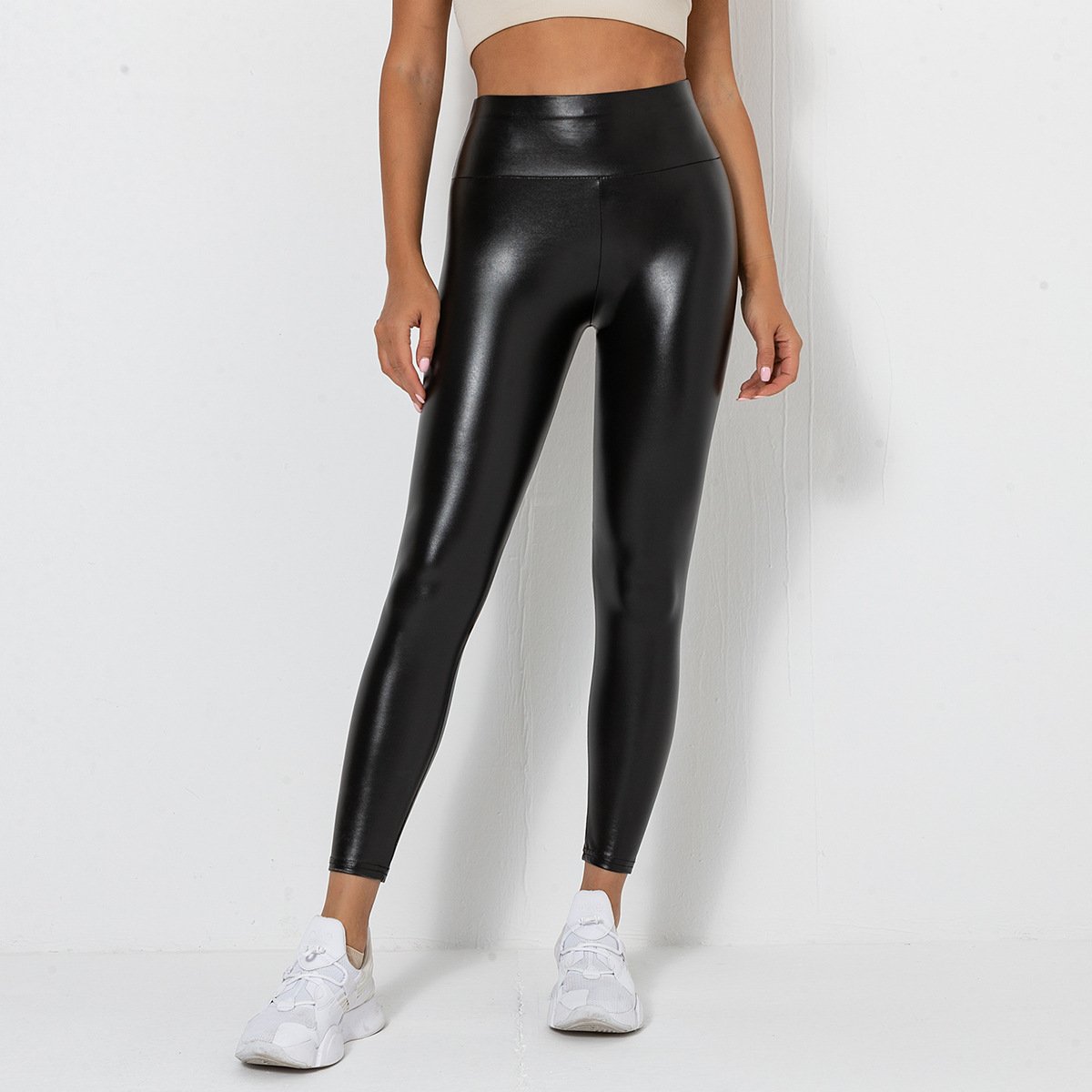 Donna in leggings neri lucidi, top beige e scarpe da ginnastica bianche. Moda fitness, abbigliamento sportivo elegante, stile casual chic.