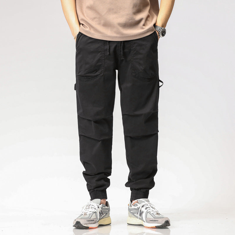 Pantaloni cargo neri da uomo con tasche multiple, indossati con sneakers bianche e grigie. Stile casual, moda maschile, abbigliamento urbano.