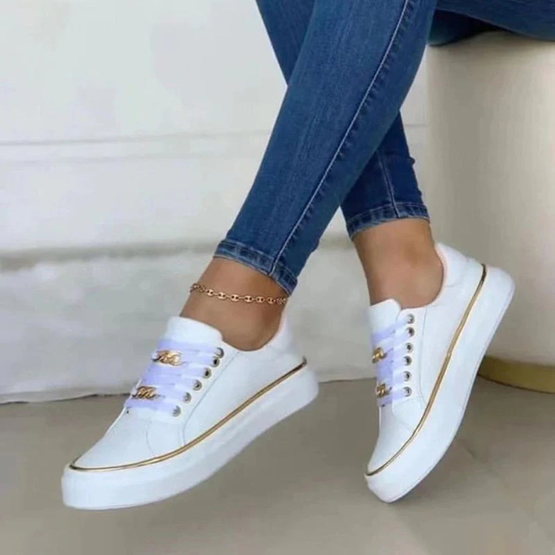 Scarpe da ginnastica bianche eleganti con dettagli dorati, indossate con jeans attillati. Scarpe casual moda donna, stile moderno e chic.