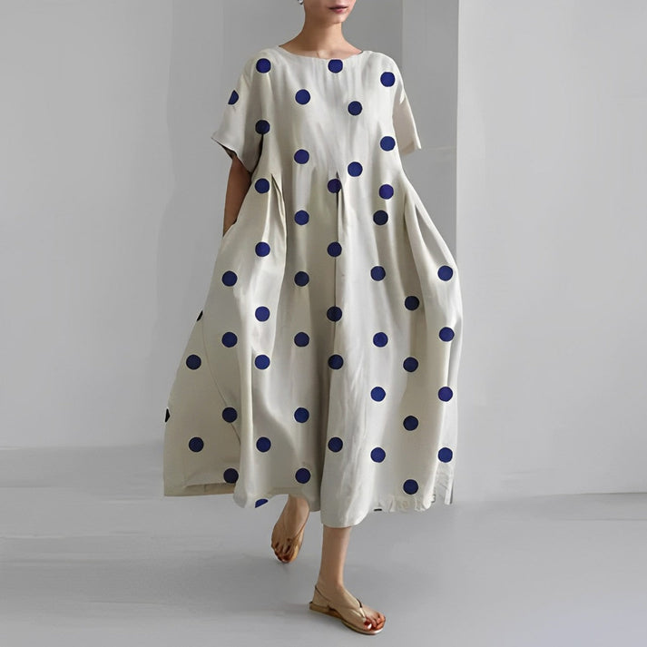 Abito lungo bianco a pois blu, stile casual, maniche corte, tessuto leggero, perfetto per l'estate. Donna con sandali beige. Moda femminile elegante.