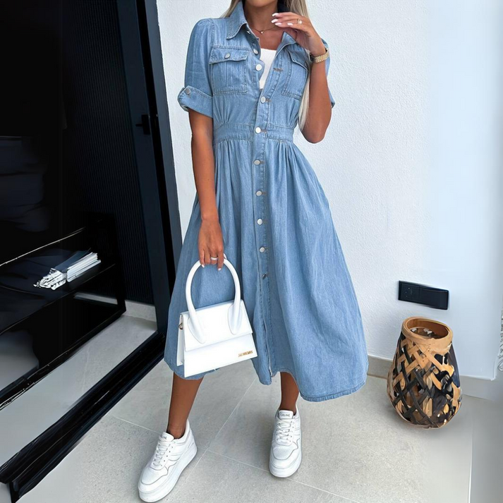 Donna in abito di jeans con bottoni, borsa bianca e sneakers, posa in interni moderni. Moda casual femminile, stile denim, tendenze abbigliamento 2023.