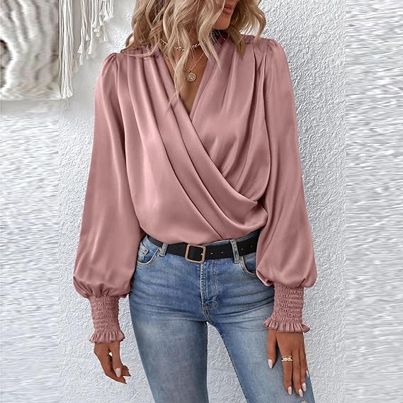 Donna con camicetta rosa satinata incrociata, maniche lunghe con polsini arricciati, abbinata a jeans chiari e cintura nera. Moda elegante casual.